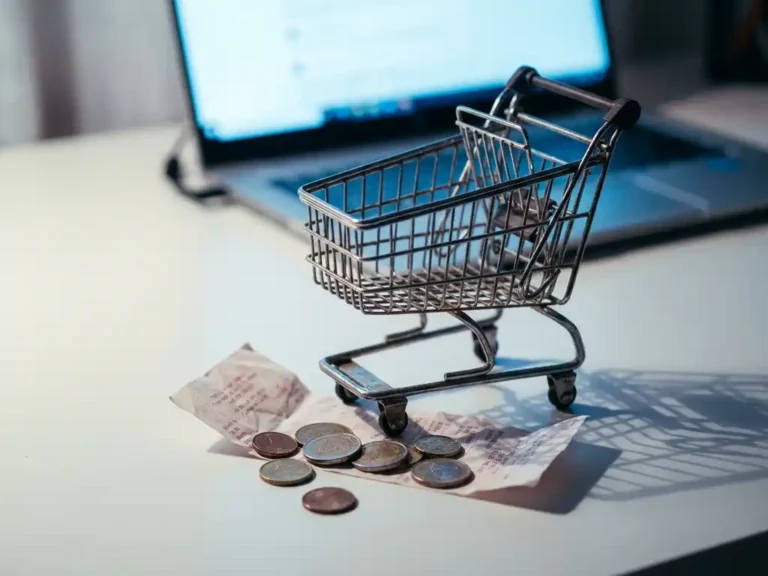 Leerer digitaler Einkaufswagen auf weißem Schreibtisch mit verstreuten Euromünzen und zerknüllten Kassenbon