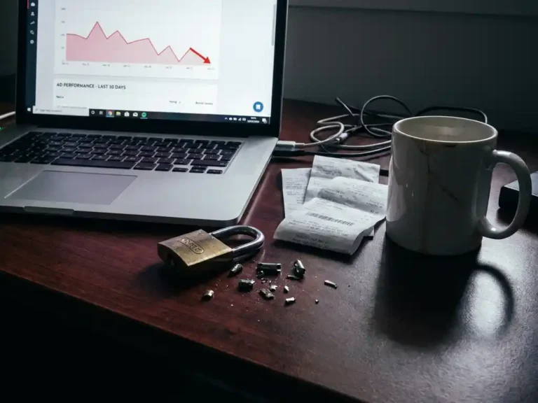 Zerbrochenes Vorhängeschloss auf einem Schreibtisch neben einem Laptop mit sinkendem Werbe-Performance-Diagramm und verstreuten Quittungen.